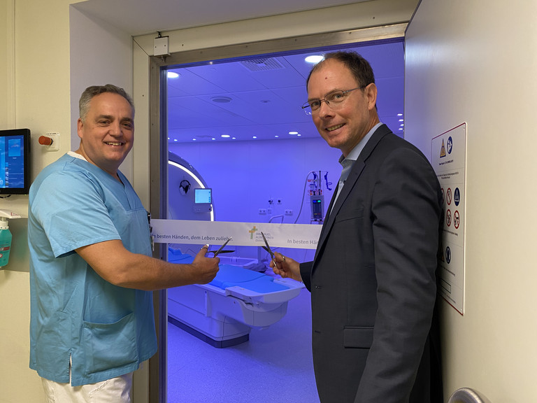 Pressefoto 2025-10-23: Evangelisches Amalie Sieveking Krankenhaus: Modernste MRT-Technologie für präzise Diagnostik und mehr Patientenkomfort Chefarzt Prof. Christoph Weber und Geschäftsführer Andreas Schneider schneiden das Band vor dem dunkelblau illuminierten Raum mit dem neuen MRT-System im Immanuel Albertinen Zentrum für Radiologie am Standort Ev. Amalie Sieveking Krankenhaus in Hamburg durch