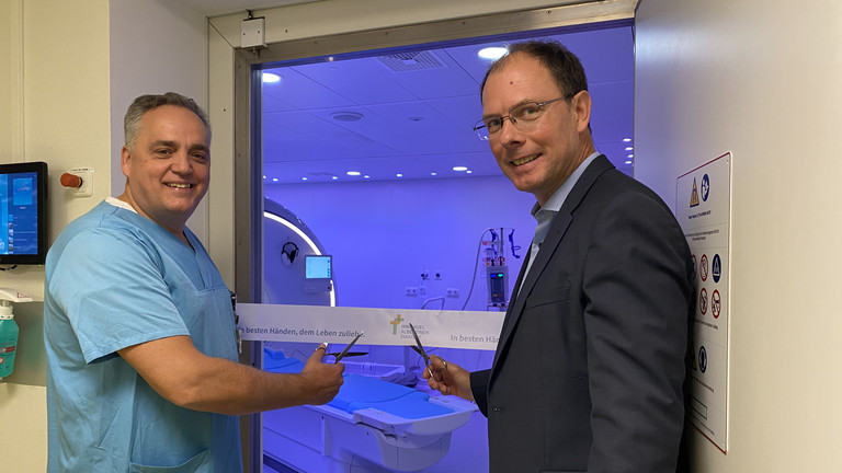 Chefarzt Prof. Christoph Weber und Geschäftsführer Andreas Schneider schneiden das Band vor dem dunkelblau illuminierten Raum mit dem neuen MRT-System im Immanuel Albertinen Zentrum für Radiologie am Standort Ev. Amalie Sieveking Krankenhaus in Hamburg durch